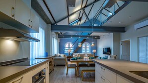 Una cocina moderna con armarios de madera, un comedor con mesa y sillas, y una escalera que conduce a un nivel superior.