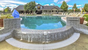 Piscina com borda curva, cercada por um deck de pedra e uma área de estar coberta.