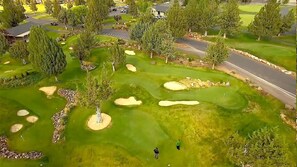 A golf course with sand bunkers, trees, and a road.