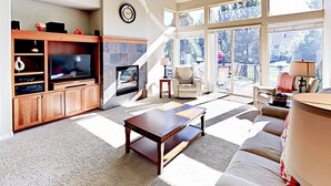 Uma sala de estar ampla com lareira, televisão e uma grande janela com vista para um deck.