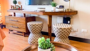 A modern living room with a wooden dining table, two woven stools, a TV, a lamp, and a potted succulent. - New Waikiki Boutique Condo 1.5 blocks to the sands of Waikiki Beach!  (Honolulu)