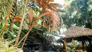 A serene garden with a rock formation, a small waterfall, and a thatched-roof structure. - New Waikiki Boutique Condo 1.5 blocks to the sands of Waikiki Beach!  (Honolulu)