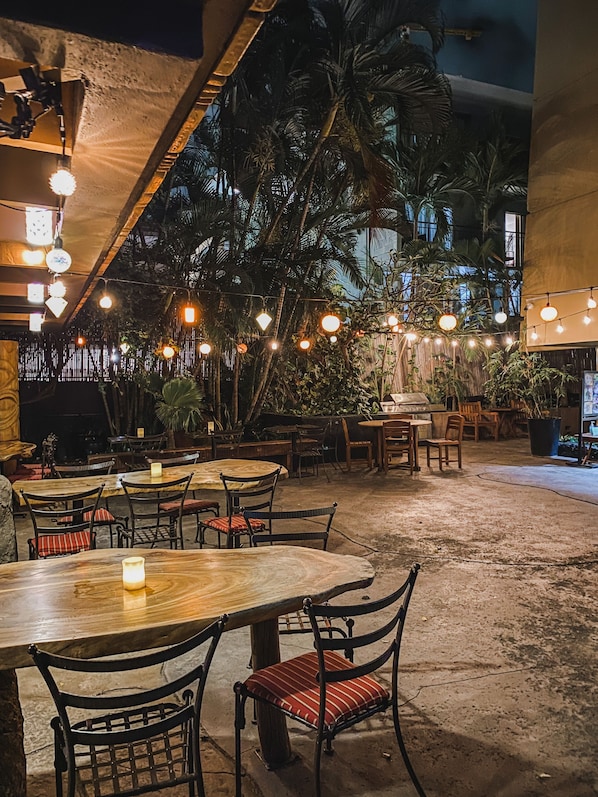 An outdoor dining area with tables and chairs, string lights, and tropical plants.