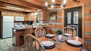 Interior de una cabaña de madera con comedor, cocina y un gran ventanal.