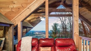 Un interior de madera con un sofá de cuero rojo, vistas de un pueblo a través de amplios ventanales y un techo de madera.