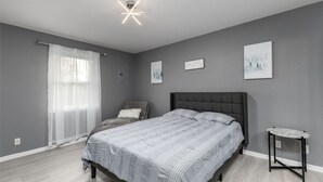 Un dormitorio con cama, una silla, una mesita y obras de arte en las paredes.