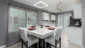 Una cocina moderna con armarios blancos, encimera de mármol y zona de comedor con una mesa para dos personas.