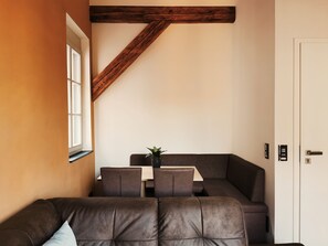 Un salon chaleureux avec un canapé en cuir marron, une poutre en bois au plafond, une petite table sur laquelle est posée une plante, et une porte blanche.