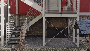 Um edifício com vários níveis, uma escadaria de cor branca, uma parede de pedra e fachada vermelha.