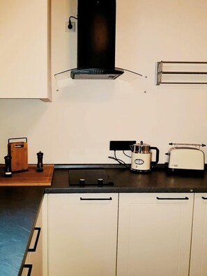 Une cuisine avec des meubles blancs, une hotte noire, une machine à café et un grille-pain.