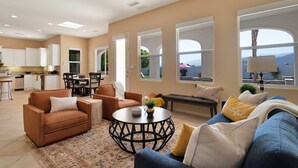 A spacious living area with a sofa, coffee table, and a dining table. There are large windows providing a view of the outdoors.