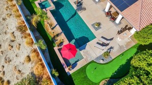 An aerial view of a property with a swimming pool, a tennis court, and a covered patio area with seating.
