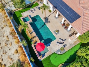 Vue aérienne d’une propriété dotée d’une piscine, d’un court de tennis et d’un patio couvert aménagé avec des sièges.