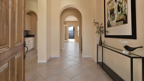 A hallway with a wooden door, a kitchen area, and a framed artwork on the wall.