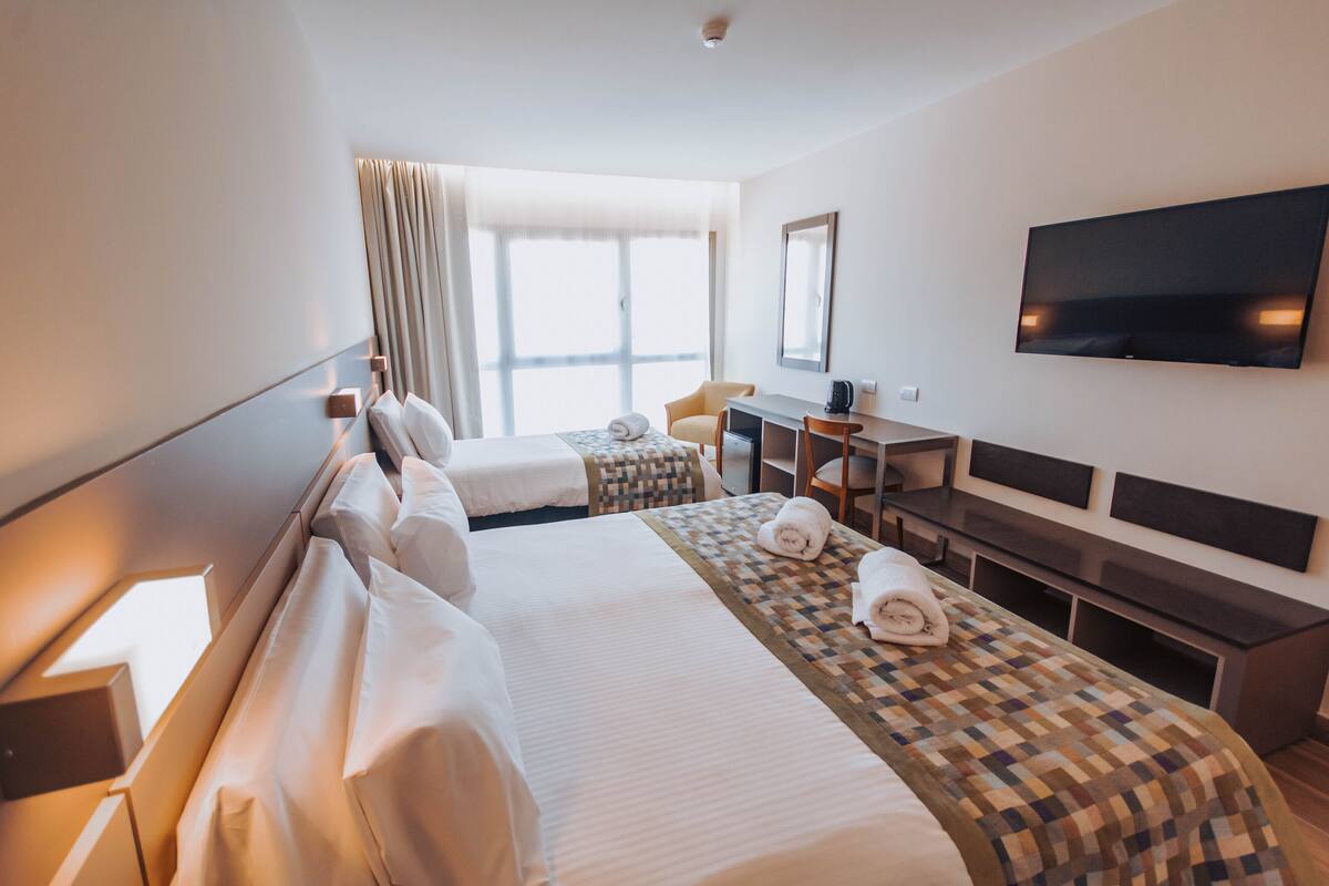 Ein Hotelzimmer mit zwei Betten, einem Schreibtisch, einem Stuhl, einem Fernseher und einem großen Fenster.