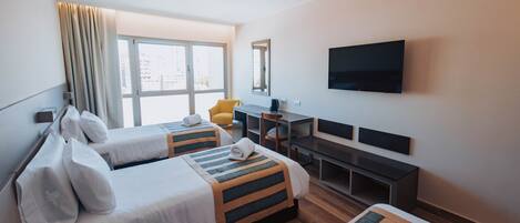 A hotel room with two beds, a desk, a chair, a TV, and a window with curtains.