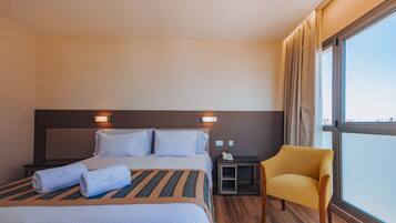 Hotelkamer met een groot bed, twee nachtkastjes, een stoel en een raam met gordijnen.