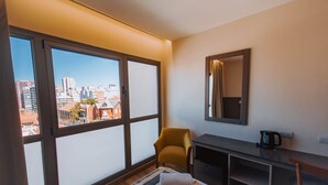 Ein Hotelzimmer mit großem Fenster, Schreibtisch, Stuhl und einem kleinen Tisch mit Wasserkocher.
