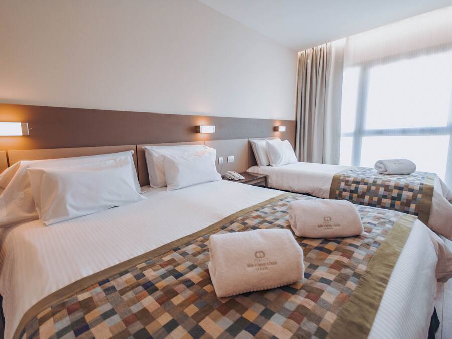 A hotel room with two beds, a check-in desk, and a large window with curtains.