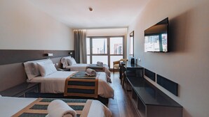 Ein Hotelzimmer mit zwei Betten, einem Schreibtisch, einem Stuhl und einem an der Wand befestigten Fernseher.