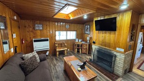Un interior acogedor de cabaña con paredes de madera, una chimenea, un televisor montado en la pared y un sofá con cojines.