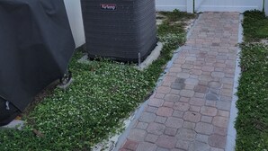 Een buitenunit van Airtemp naast een wit hek, met een overdekte barbecue en een verhard pad dat naar een hekkenpoort leidt.