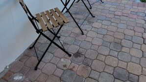 Een terras met twee houten tafels en stoelen, een geplaveid terras en een houten omheining op de achtergrond.