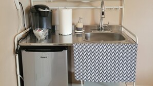 Een compacte kitchenette met een magnetron, koffiezetapparaat en kleine koelkast.
