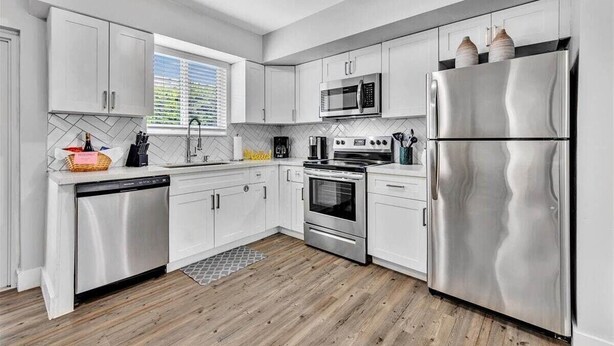 A modern kitchen with white cabinets, stainless steel appliances, and a wooden floor. - 3Bed Modern Home Family Friendly Heated Pool (Fort Lauderdale)