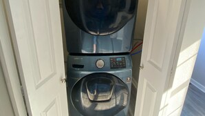 A compact laundry room with a front-loading washer and dryer, a control panel, and a door leading to another room. - New!! Woodcrest Cottage - Close to Tri-Cities (Kingsport)