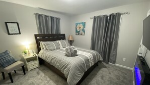 A bedroom with a bed, nightstands, a lamp, a TV, and grey curtains. - New!! Woodcrest Cottage - Close to Tri-Cities (Kingsport)