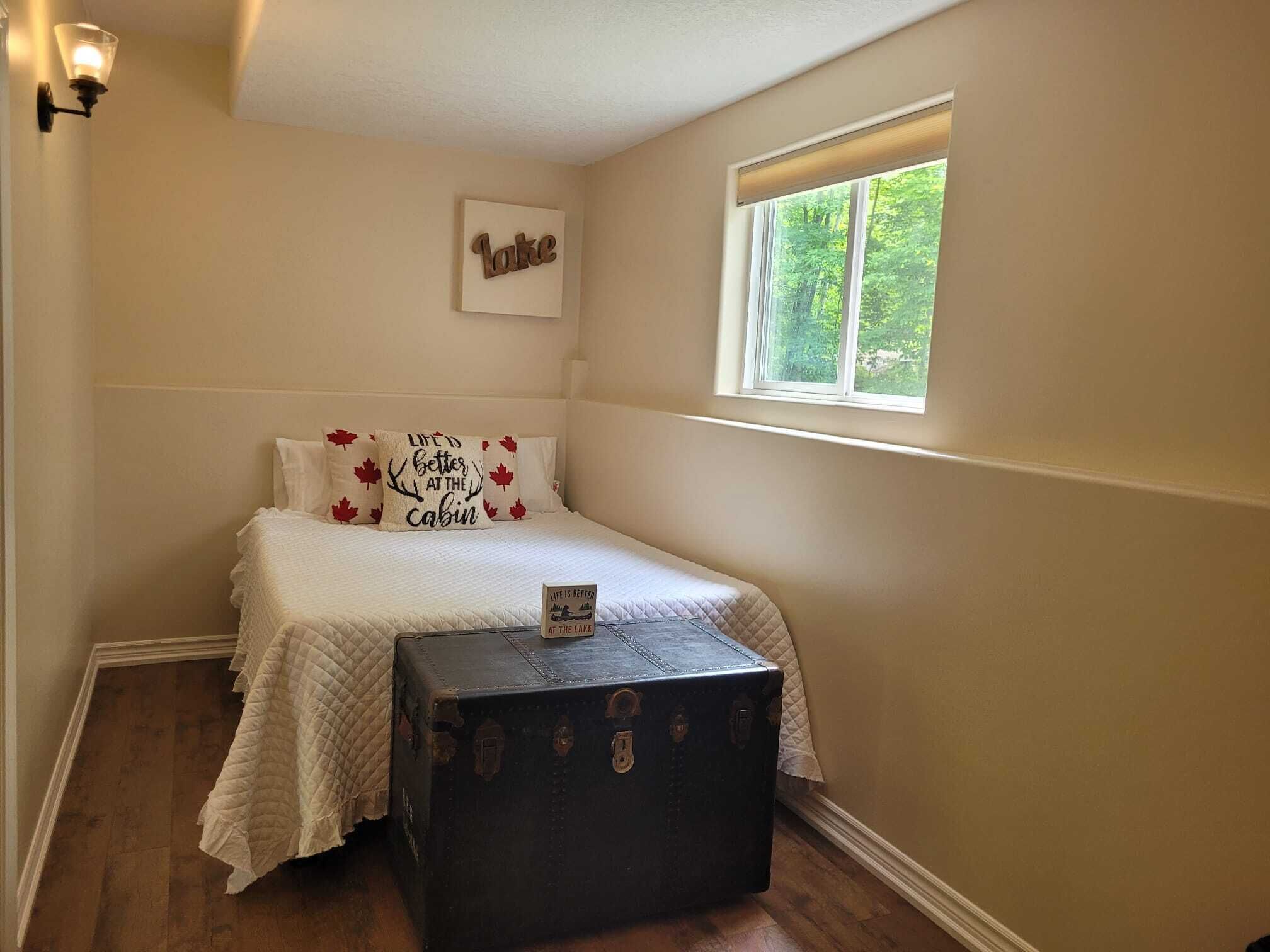 Un dormitorio con cama, ventana, luz instalada en la pared y maleta.