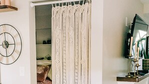 Una puerta con cortina de macramé, un reloj, un televisor y una planta en maceta.