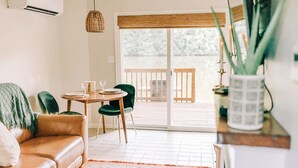 Una sala de estar con un sofá de cuero marrón, una mesa redonda de madera con dos sillas y un gran ventanal corredero que da a una terraza exterior.