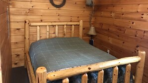 Ein Zimmer in einer Holzhütte mit einem Bett, einer Wandlampe und einem Kranz an der Wand.