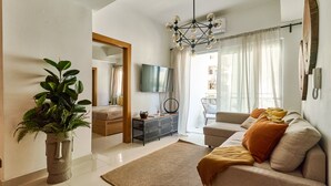 Un salon avec un canapé, une table basse, un téléviseur et une grande plante.