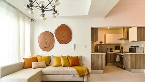 Un salon moderne avec un canapé d’angle, un tapis tissé et une cuisine dotée de meubles en bois et d’un four encastré.