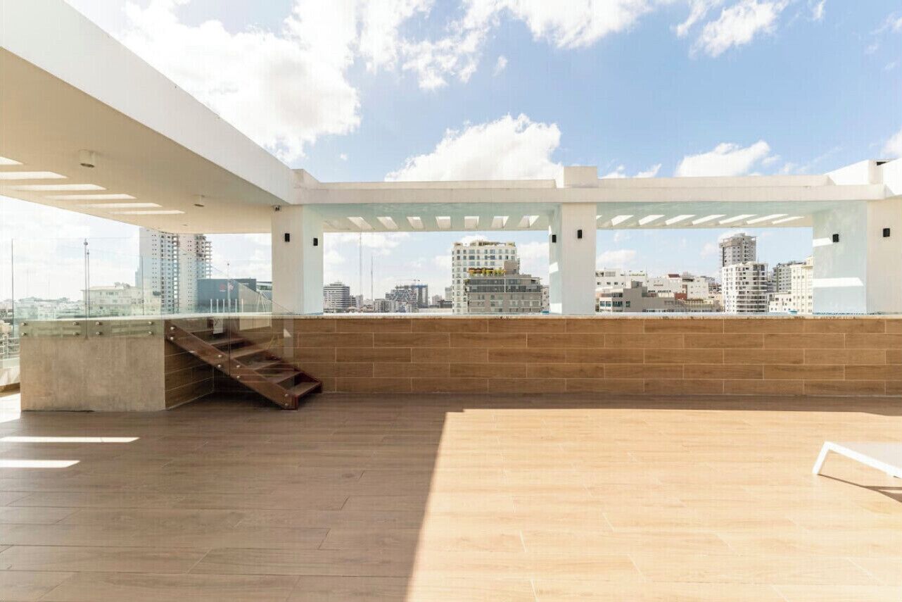A spacious rooftop terrace with a city view, a concrete staircase, and a glass railing.