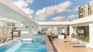 Une piscine sur le toit, dotée de chaises longues et offrant une vue sur la ville.
