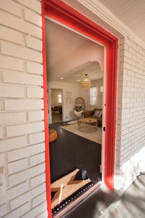 A doorway leading into a room with a patterned rug, a round table, and a wicker chair.