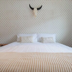 A bed with a patterned blanket, two pillows with geometric designs, and a wall with a geometric pattern.