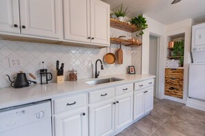 A kitchen with white cabinets, a sink, a coffee maker, and a plant on a shelf.