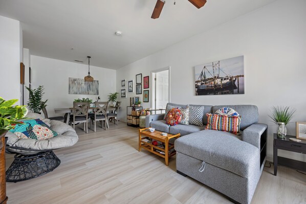 A spacious living area with a grey sofa, a wooden coffee table, and a dining area with a table and chairs.