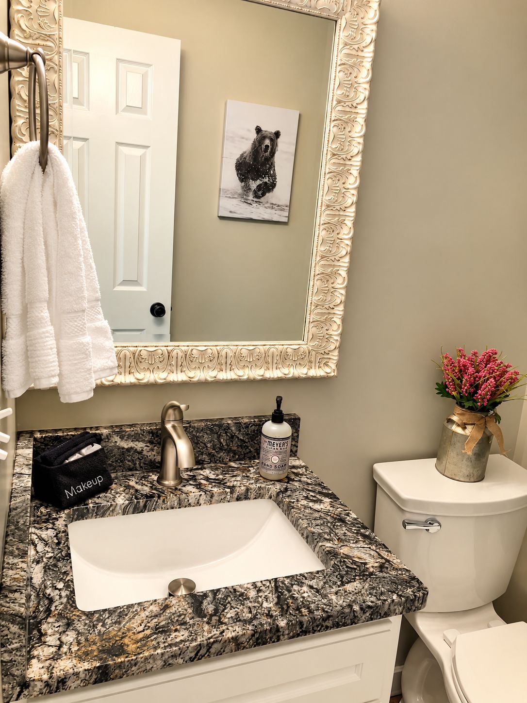 Ein Badezimmer mit Marmorplatte, Waschbecken, Toilette, Handtuchhalter, einem gerahmten Bild und einer Blumenvase.