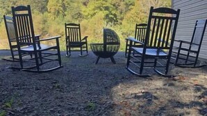 A patio with four rocking chairs and a round table, surrounded by a forested area.