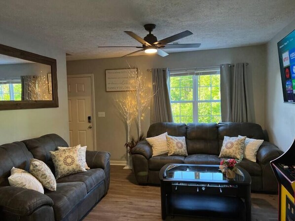 A living room with two dark leather sofas, a glass coffee table, a ceiling fan, a decorative tree, and a window with curtains. - RARE - 2 miles to Dollywood - Arcades & Much More (Sevierville)
