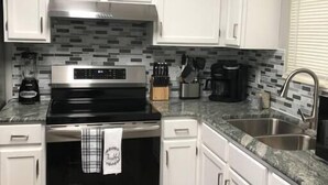 A kitchen with white cabinets, a stainless steel range, a tiled backsplash, and a granite countertop.