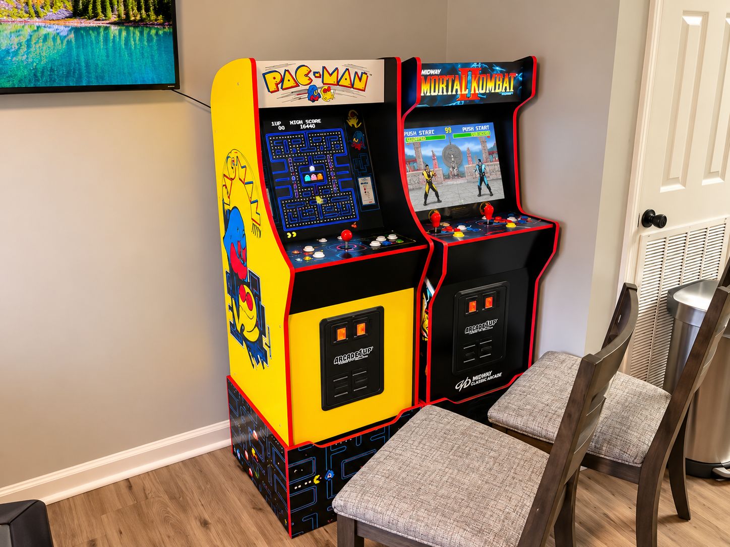Two arcade machines, one labeled 'PAC-MAN' and the other 'MIDWAY MORTAL KOMBAT,' with a small table and two chairs in front.