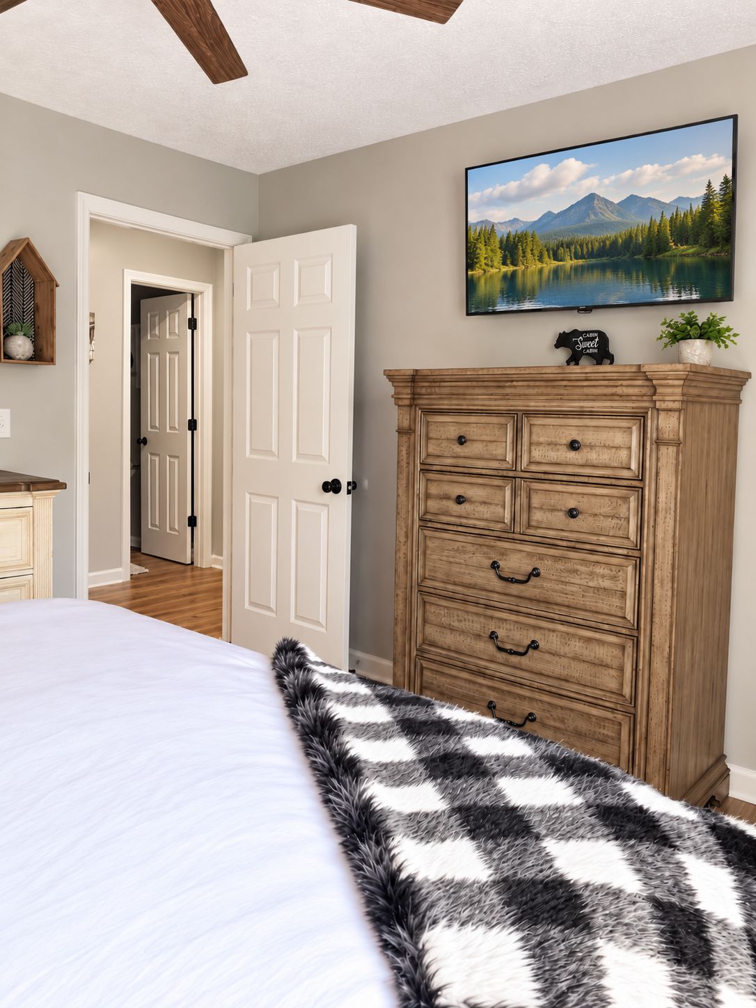 A bedroom with a bed, a dresser, a painting, and a door leading to another room.
