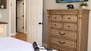 A bedroom with a bed, a dresser, a painting, and a door leading to another room.